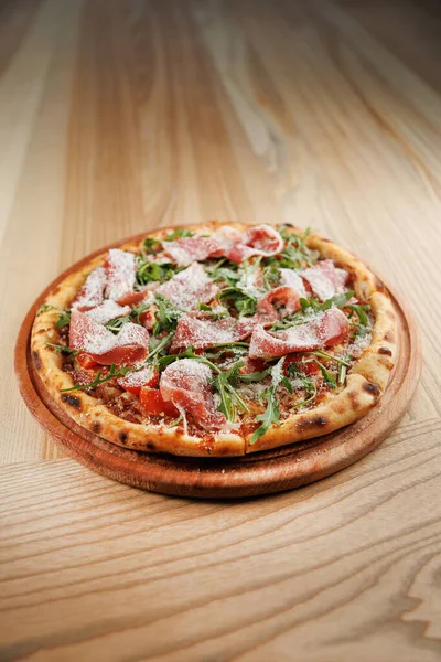 Yuvarlak pizza, domates soslu ince bir kabuk, pişirilmiş et dilimleri ve taze roka içerir. Tahta servis tahtasının üzerinde duruyor, canlı renklerini ve dokularını sergiliyor..