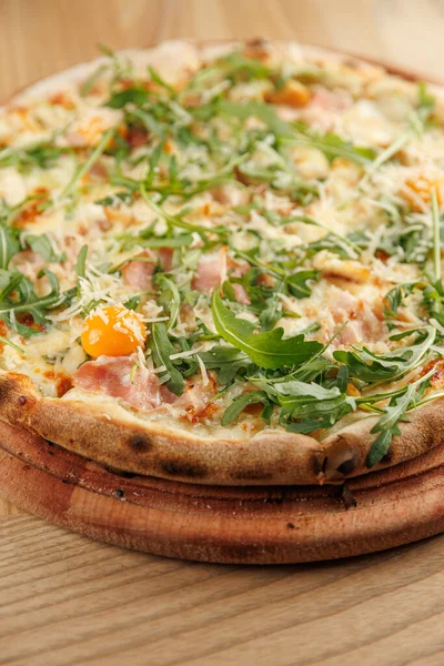 Tahta üzerinde roka, jambon, peynir ve yumurta bulunan ahşap kaplı bir pizza. Paylaşmak ya da yalnız eğlenmek için mükemmel.