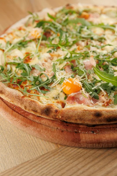 Tahta bir tahtada jambon, peynir ve taze yeşillik ile bir pizza sunulur. Yemek merkezinde canlı bir yumurta sarısı sergiliyor. Sıradan bir lokantada servis yapmaya hazır..