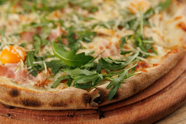 İnce hamurlu pizza taze ve roka, peynir ve jambon malzemeleriyle iştah açıcıdır. Tahtaya yerleştirilmiş, eğlenmeye hazır..