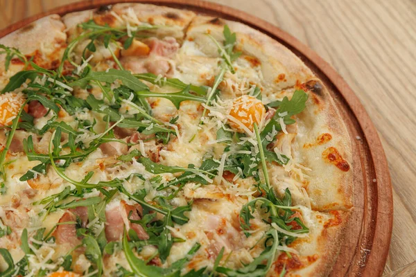 Tahta üzerinde et, peynir ve yeşillik gibi malzemelerle servis edilen bir pizza. Kabuğu altın ve çıtır çıtır. Her ısırıkta farklı mutfakların tadını çıkar..