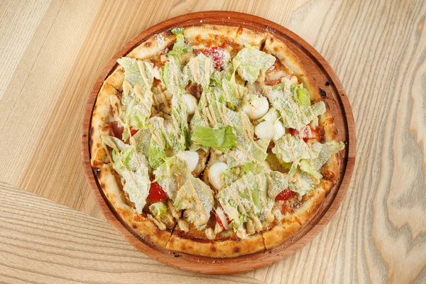 Yuvarlak bir pizza marul, domates ve bir tutam peynirle kaplıdır. Tahta bir tabakta sunuluyor. Ayar hafif ahşap yüzeylere sahiptir..