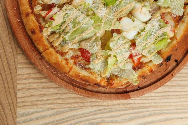 Marul, tavuk ve sosla kaplı taze pizza ahşap servis tahtasının üzerinde duruyor. Tat ve malzemelerin karışımının tadını çıkarın. Aşçılık gelenekleri sergileniyor..