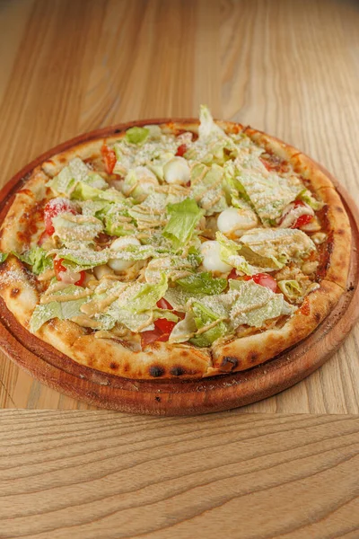 Marul, domates ve peynirle kaplı yuvarlak bir pizza ahşap servis tahtasına yerleştirilir. Arkadaşlarla ya da ailelerle sıradan bir yemek ortamında eğlenmeye hazır görünüyor..