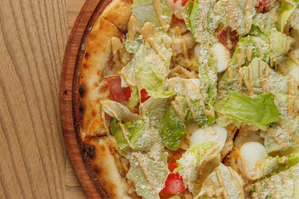 Yeşillik, domates ve peynirli bir pizza ahşap bir tahtanın üzerinde duruyor. Bu yemek farklı aşçılık geleneklerinden öğeler sergiliyor. Bu da onu yemek sevenler için hoş bir seçim yapıyor..