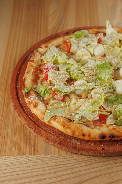 Kıtır kenarlı bir pizza marul, domates ve peynirle kaplıdır. Sıcak, davetkar bir restoranda ahşap bir yüzeye oturur. Bu yemek arkadaşlarla paylaşmak için mükemmel..