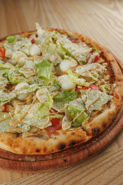 Yeni pişmiş bir pizza ahşap servis tahtasına yerleştirilir. Pizza dilimlenmiş marul, domates ve peynirle kaplı, öğle yemeği veya akşam yemeği için hazır..