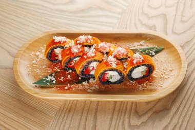 Ahşap bir tabağa konmuş renkli malzemeler ve malzemeler sergilenen suşi ruloları. Yemek bir Japon yemek alanında özenle düzenlenmiştir..