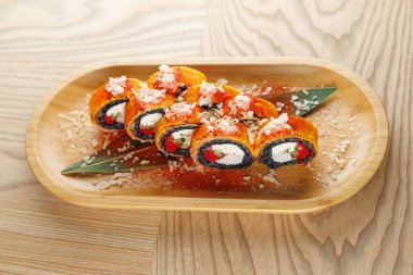 Suşi ruloları ahşap bir tepside güzelce sergileniyor pirinç, deniz ürünleri ve malzemeler gibi malzemelerin katmanlarını gösteriyor. Yemek aşıkları Japon mutfağının tadını tatmak için davet edilir..