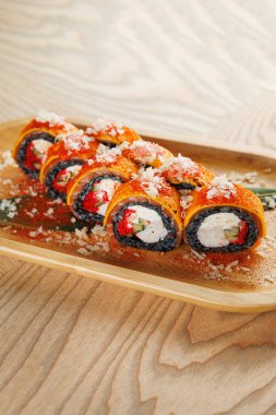 Ahşap bir tabakta sebze ve krem peynirle dolu ve malzemelerle süslenmiş çok sayıda canlı suşi ruloları yer alıyor. Yemek sırasında keyif almak için güzelce düzenlenir..