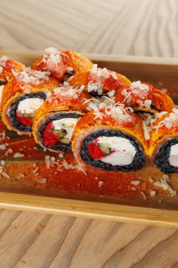 Krem peynir, sebze ve dilimlenmiş deniz ürünleri ve baharatlarla dolu suşi ruloları bir restoran masasında ahşap bir tabakta sunuluyor..