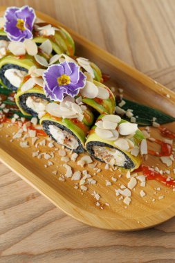 Suşi ruloları bambu tepsisinin üzerine güzelce dizilir. Üstleri çiçeklerle ve dilimlenmiş bademlerle kaplı. Tabağı süsleyen sos serpintileriyle. Ayar gündelik ve davetkar..