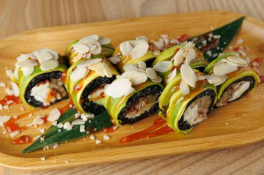 Suşi, badem dilimleriyle kaplı deniz yosununa sarılı tavuk ve avokado sarar. Tahta tepside sunuluyorlar, lezzet arttırıcı sosla birlikte..