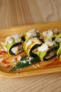 Taze malzemelerle yapılan suşi ruloları ahşap bir tabakta sunulur. Ekmekler badem dilimleriyle kaplı ve baharatlı sosla süslenmiş..