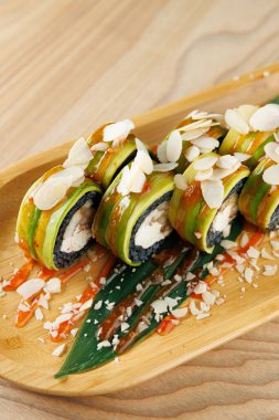 Taze avokadoyla yapılmış suşi ruloları ve badem dilimleriyle kaplanmış bambu tepsisi üzerinde oturuyorlar. Sos serpiştirilmiş bu yemek Japon aşçılık becerilerini sergiliyor..