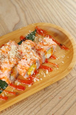 Suşi ruloları domates sosu ve malzemelerle ahşap bir tabağa konur. Dekor parlak, tabakları aydınlatıyor. Bu yemek Japon mutfağının özünü yansıtıyor..