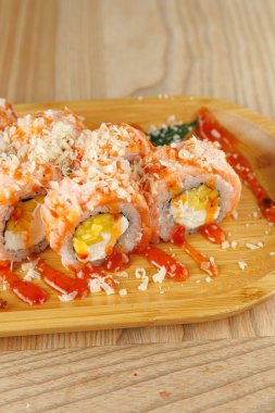 Suşi dürümleri ahşap bir tabakta servis edilir. Baharatlı sos ve çıtır çıtır gevreklerle süslenmiş balık ve dolgu tabaklarıyla lezzetli bir yemek için..