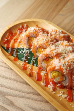 Pirinç, balık ve sebzelerden yapılmış güzel bir suşi rulosu ahşap bir tabakta oturur. Sos ve malzemeler sunumu güçlendirir. Bu yemek suşi severler için mükemmel..