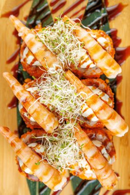 Lezzetli karides suşi ruloları ahşap bir tabakta düzenlenir. Tabakta sos ve filizler yer alıyor, canlı bir tat ve doku karışımı sergiliyor..