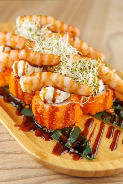 Karides suşisi portakal yumurtası ve ahşap tabakta kremalı sos içerir. Taze malzemeler arasında suşi hazırlama becerisini gösteren lahanalar ve deniz yosunu da var..