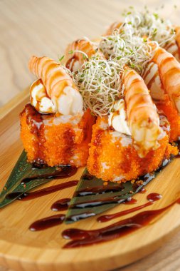 İçinde karides, portakal yumurtası ve lahanaların olduğu suşi tabağının detaylı bir görüntüsü. Suşi ahşap bir tahtanın üzerine serpiştirilmiş..
