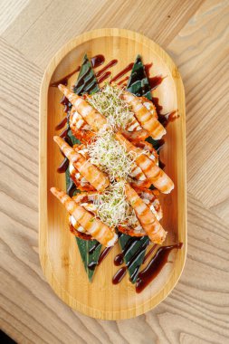 Üzerine ızgara karides konmuş taze suşi garnitür ve süsleme sosuyla bambu tabağında düzenlenir. Bu yemek sizi canlı lezzetlerden ve dokulardan zevk almaya davet ediyor..