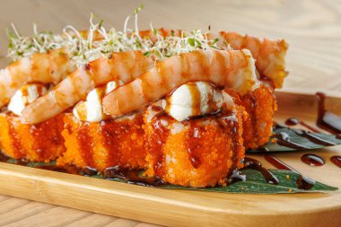 Karides ve tobiko suşi ruloları ahşap bir tabakta, lahanalarla kaplı ve sosla sergileniyor. Bu yemek, deniz ürünleri aşıkları için mükemmel..