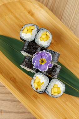 Mango dilimleri ve pirinçle dolu taze suşi ruloları bambu tabağa konur. Mor bir çiçek renk katar, bu da yemeği restoran müşterilerine cazip hale getirir..
