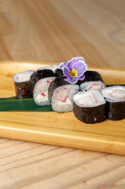 Suşi ruloları üzerinde narin bir çiçek bulunan ahşap bir tabakta düzenlenir. Ekmekler pirinç ve taze balıktan yapılıyor. Japon mutfak sanatı sergileniyor..