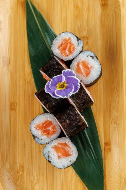 Taze somonla dolu suşi ruloları bambu bir tahtada düzenlenir. Narin bir çiçek yeşil bir yaprağın üzerinde oturur, tabağa biraz renk katar..