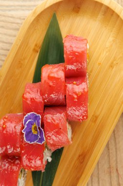 Taze ton balığı suşisi bambu bir tabakta düzenlenir ve üzerinde yenilebilir bir çiçek bulunur. Yemek sunumuna vurgu yaparak basit bir yemek masası atmosferi sergiliyor..