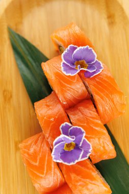 Somon balığı parçaları ahşap bir tabakta güzelce düzenlenir. Her parça mor çiçeklerle süslenmiş, Japon mutfağındaki detaylara dikkat çekiyor..