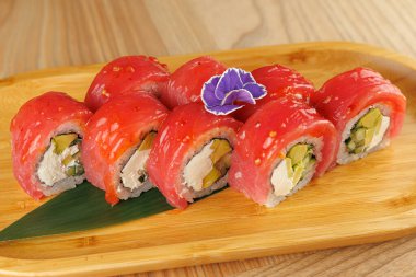 Renkli suşi dürümleri ahşap bir tahtada güzelce düzenlenir. Her rulo taze malzemeler ve canlı malzemeler içeriyor. Sahne eğlenmeye hazır bir yemek gösteriyor..