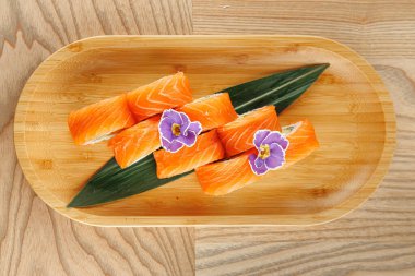 Taze somon balığı yeşil yapraklar ve mor yenilebilir çiçeklerle bambu bir tabakta sergilenir. Sunum yemek deneyimine biraz renk katıyor..