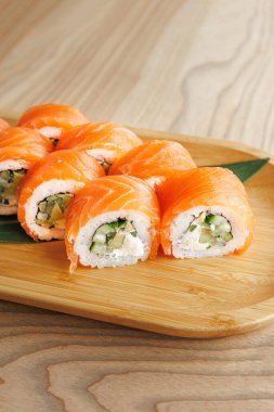 Tahtada somon ve salatalıktan yapılmış taze suşi ruloları sergileniyor. Bu yemek Japon mutfağı sanatını gözler önüne seriyor, öğle veya akşam yemeği için hazır..