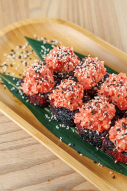 Tahta bir tabakta pembe balıklarla kaplı suşi ruloları ve susam tohumları serpiştirilir. Ayarlar basit, yemek hazırlama sürecindeki dikkati vurguluyor.