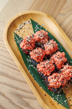 Tabaklarda farklı kültürlerden canlı renklerde çeşitli tatlar sergileniyor. Yemek ahşap bir tepside, yeşil yapraklar ve garnitür olarak serpiştirilmiş susam tohumlarıyla güzelce düzenlenmiş..