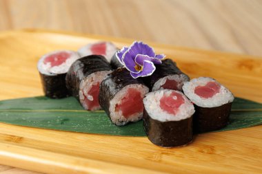 Tahta bir tahtanın üzerinde düzgünce dizilmiş ton balığıyla dolu taze suşi ruloları. Küçük bir çiçek, Japon mutfağını ve renkli sunumunu sergiliyor..