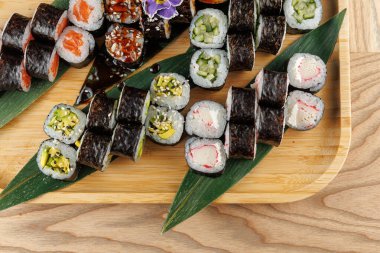 Çeşitli dolgularla suşi ruloları taze yeşil yapraklarla bambu tepsisinin üzerinde düzgünce düzenlenir. Bu ekran, rulolardaki çeşitli renk ve dokuları vurgular.