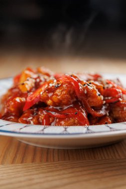 Tatlı ve ekşi tavuk kırmızı biber ve susam tohumlarıyla kaplıdır. Tabaktan dumanlar yükseliyor, bu da yeni hazırlandığını gösteriyor. Tadı ile canlı bir aşçılık deneyimi yaşamak.