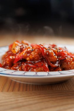 Kırmızı biber şeritleri ve susam tohumlarıyla kaplı, zengin bir sosla kaplanmış, canlı, ısırık büyüklüğünde parçalar ahşap bir masada basit bir kasede servis ediliyor..