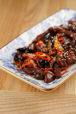 A flavorful dish showcases tender beef pieces cooked with colorful vegetables, topped with sesame seeds and presented on a decorative plate.