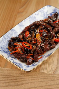 Bir tabakta mantar, biber ve susam tohumlarıyla pişirilmiş ızgara sığır eti şeritleri yer alıyor. Yemek, Ukrayna ve Japon mutfak teknikleri ve tatlarının karışımını vurguluyor..