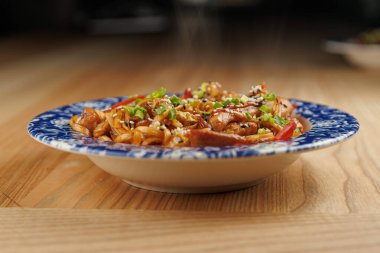 Bir tabak farklı mutfaklardan gelen çeşitli taze ve renkli yemeklerle doludur. İçindekiler arasında et, sebze ve soslar yer almaktadır..