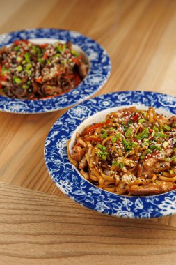 Sebzelerle dolu ve susam tohumlarıyla kaplı iki kase Asya eriştesi ahşap bir masaya yerleştirilir. Kurulum yemeğin tadını çıkarıyor..