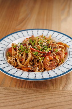 Bir tabakta yeşil soğan ve susam tohumlarıyla süslenmiş sebzeli erişte karışımı bulunur. Yemeklerde farklı küresel mutfaklardan esinlenilmiş tatlar sergileniyor..