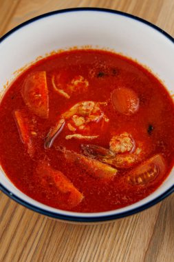 Canlı kırmızı çorbayla dolu bir kase karides, dilimlenmiş domates ve baharatlara sahiptir. Bu yemek lezzet ve taze malzemelerin karışımını sergiliyor. Her yemekten zevk almak için mükemmel..