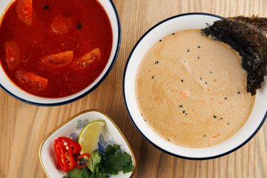 Ahşap bir yüzey üzerinde üç kase aromalı çorba farklı mutfakların yemeklerini gösteriyor. Bir kase domatesli kırmızı çorba içerirken, diğeri kremalı çorba içerir..