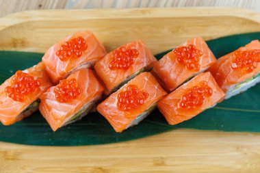 Suşi ruloları taze somon ve somon yumurtası ahşap bir tabakta güzelce sıralanır. Renkler ve dokular Japon yemek ve sunum sanatını gösteriyor..