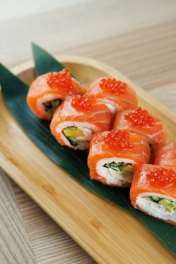 Sebze ve deniz ürünleriyle dolu suşi ruloları dikkatlice ahşap bir tabağa konur. Parlak turuncu somon balığı ve parlak kırmızı yumurta her rulonun üstünde renkli bir yemek oluşturur..